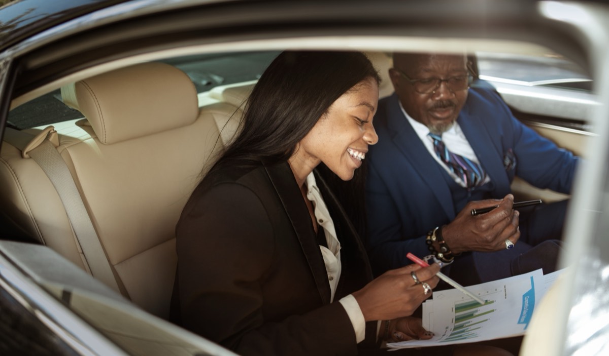 Two colleagues reviewing documents in the back of a car